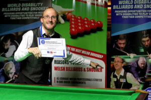 Daniel Blunn holds up his certificate after success at the Welsh Open and points to a picture of himself on a nearby banner