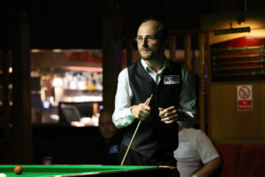 Daniel Blunn holding his cue by the table while considering a shot