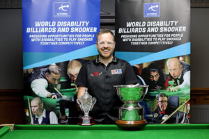 Joe Hardstaff smiles by the table with the 2023 Champion of Champions trophy